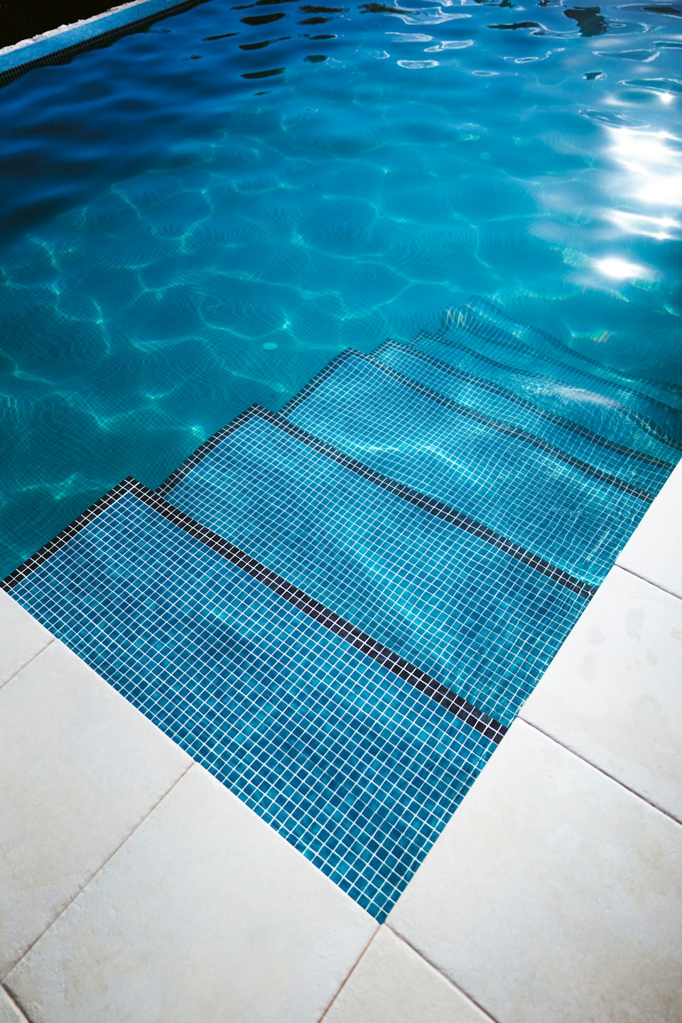Blue mosaic steps lead into a clear swimming pool.