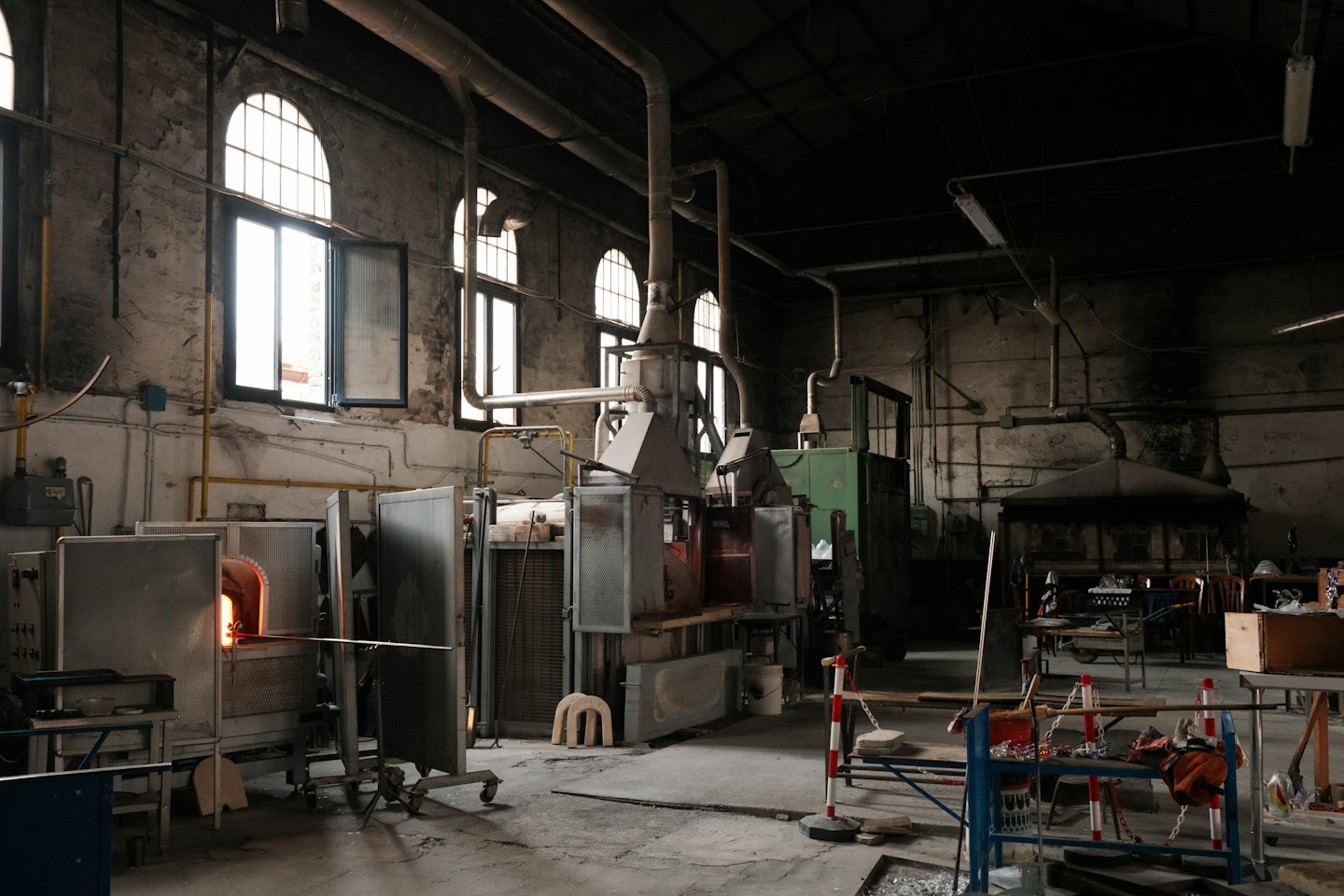 Glassblowing workshop with furnaces, machinery, and pipes.