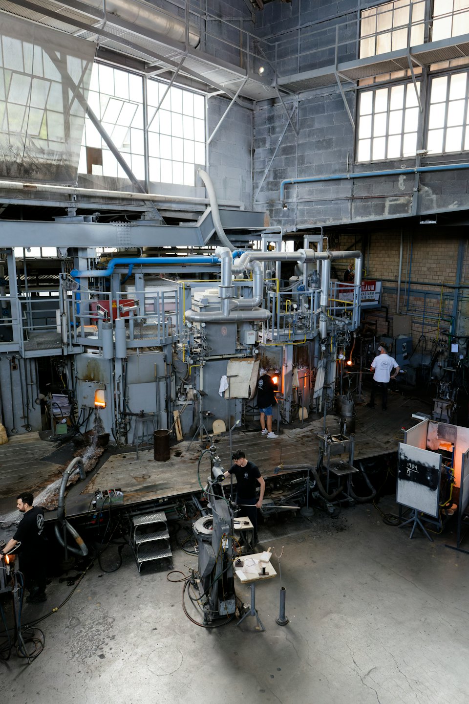 Artisans working with molten glass in a busy workshop.